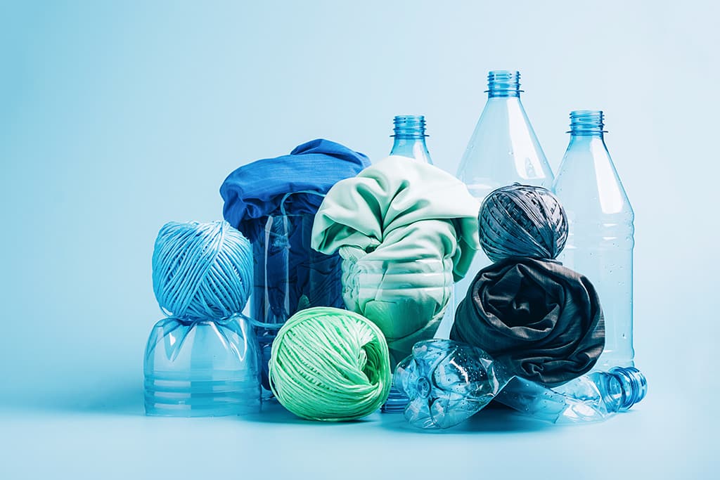 recycled polyester fiber synthetic fabric | Quincy Recycle Empty plastic bottle and various fabrics made of recycled polyester fiber synthetic fabric on a blue background
