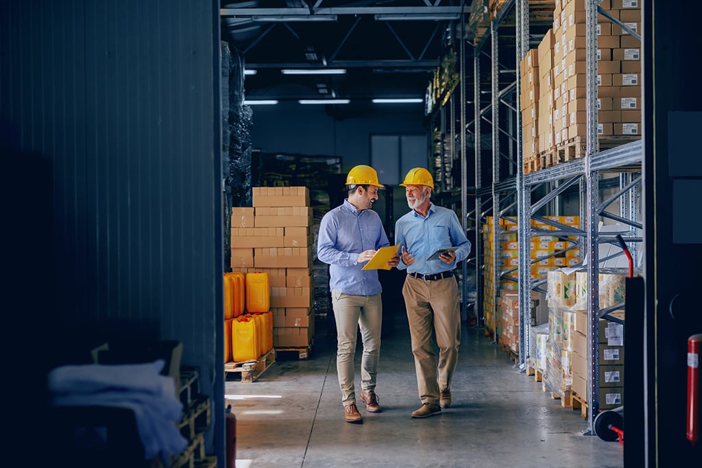 Two men wearing formal wear with protective yellow helmets on heads walking and talking about recycling business.